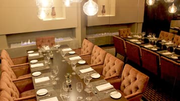 Un comedor formal con una larga mesa dispuesta para una comida, rodeada de sillones lujosos y una moderna lámpara de araña sobre ella.