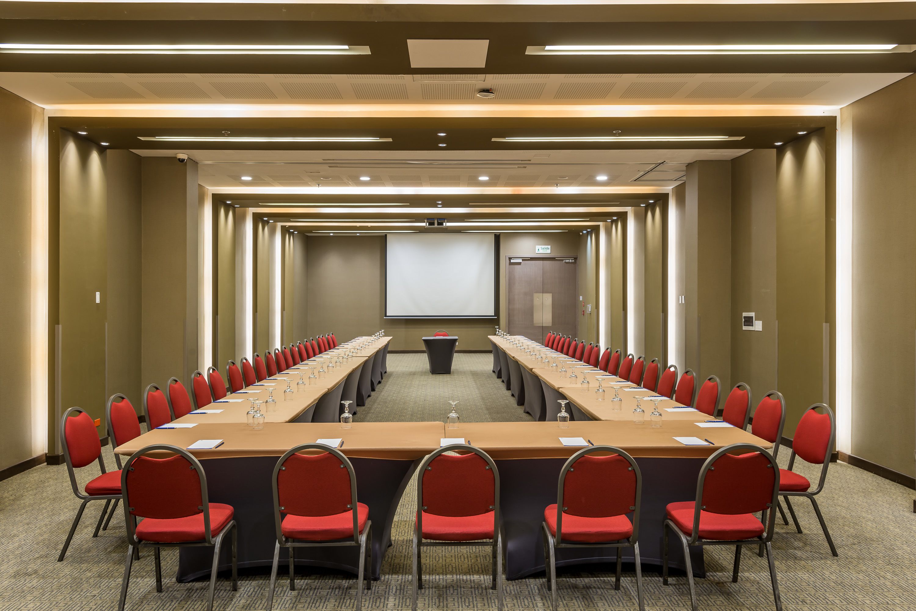 A conference room with a long table, red chairs, and a projector screen.