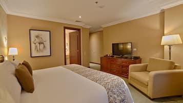 A hotel room with a large bed, a television, a sofa, and a desk with a lamp.