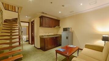Ein Hotelzimmer mit einer Holztreppe, einer Küchenzeile inklusive Holzschränke, einem Kühlschrank und einem Wohnbereich mit Sofa und Couchtisch.
