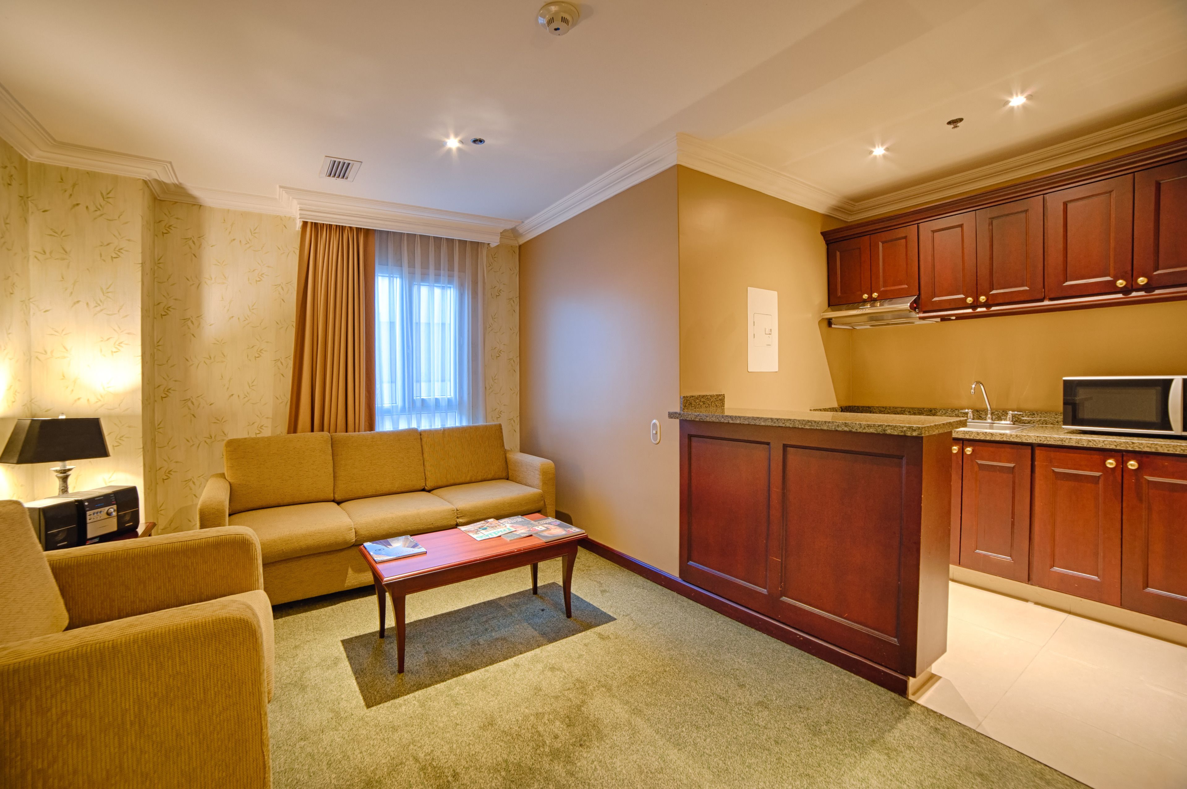 A living room with a sofa, coffee table, and a television. There is a kitchen area with wooden cabinets and a microwave.