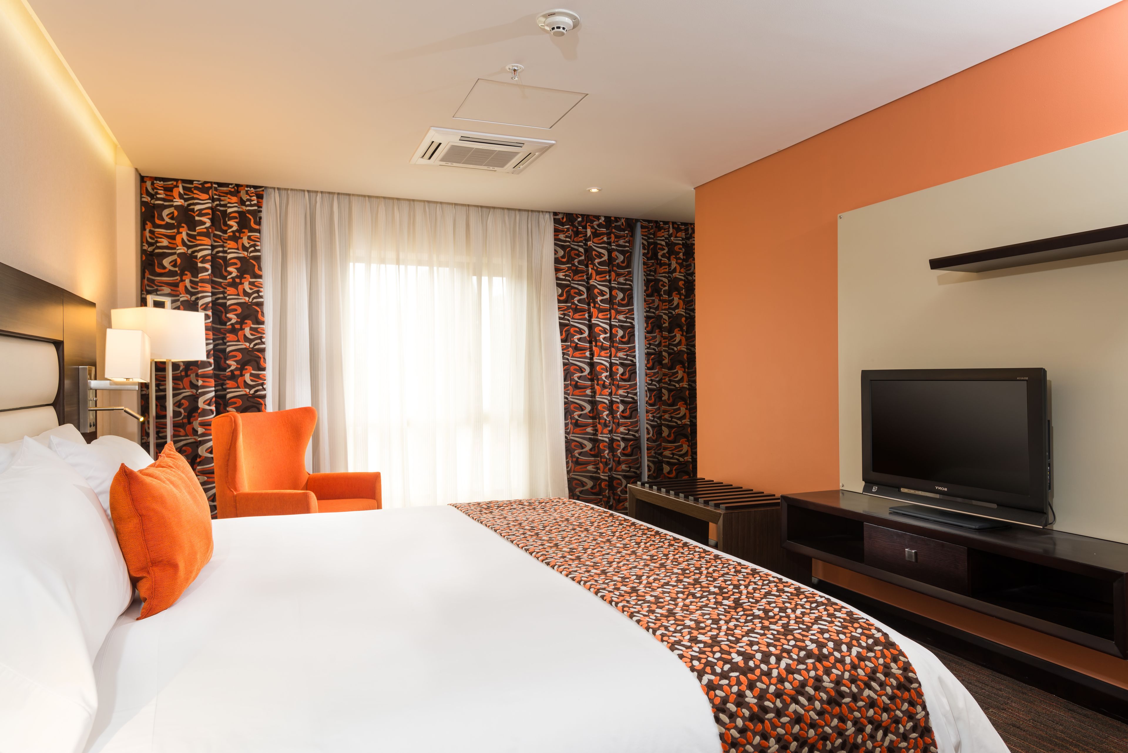 Una habitación de hotel con una cama grande, televisión, una silla y un escritorio.