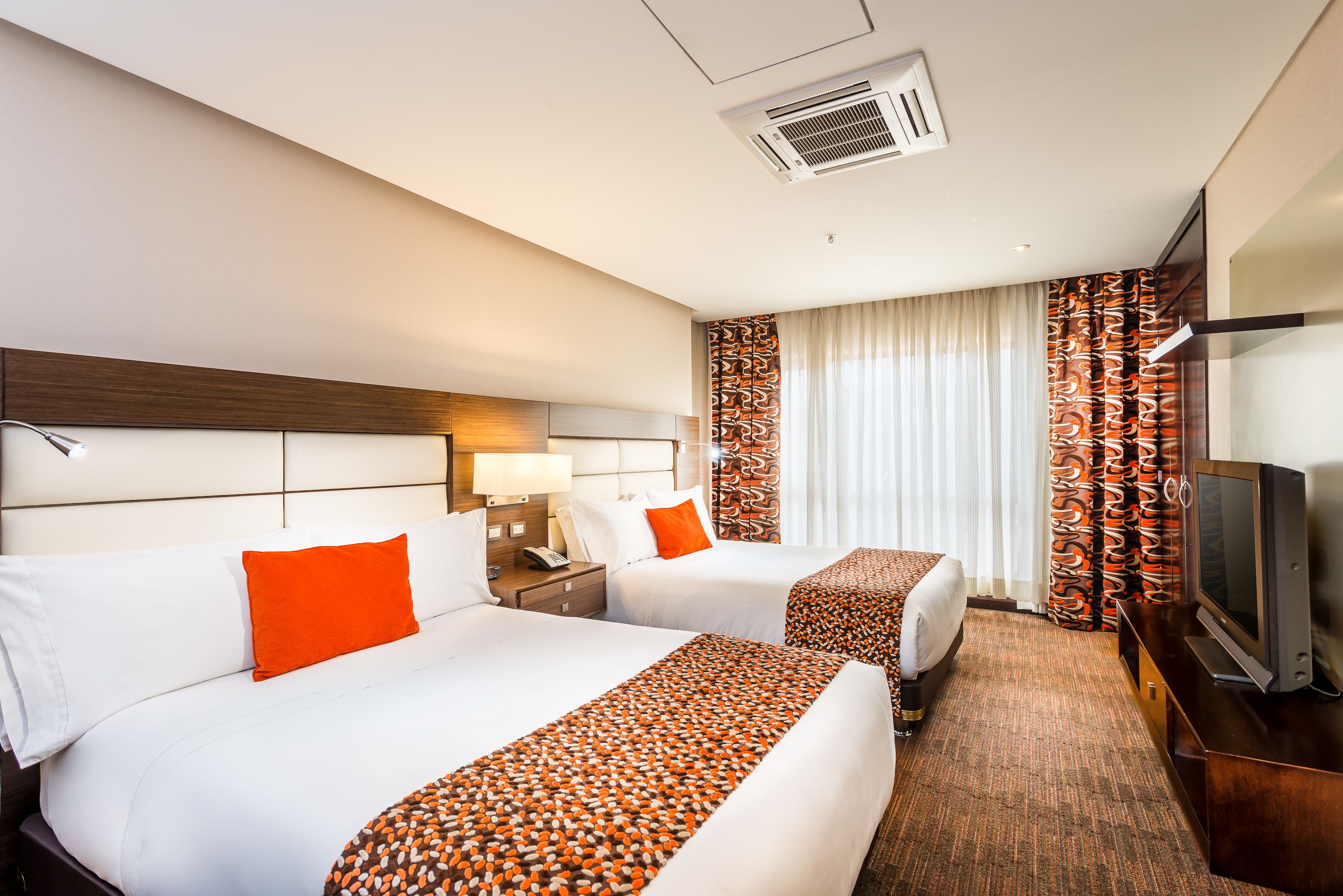 A hotel room with two beds, a TV, a desk, and a window with curtains.
