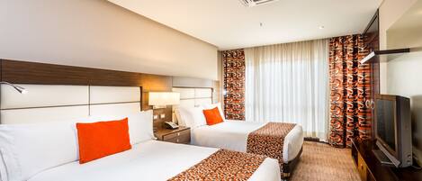 A hotel room with two beds, a TV, a desk, and a window with curtains.