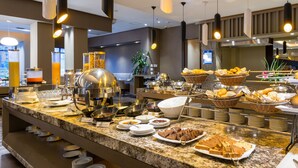 Un bufé con diferentes alimentos y utensilios de servicio, una estación de café y un área de estar con mesas y sillas.