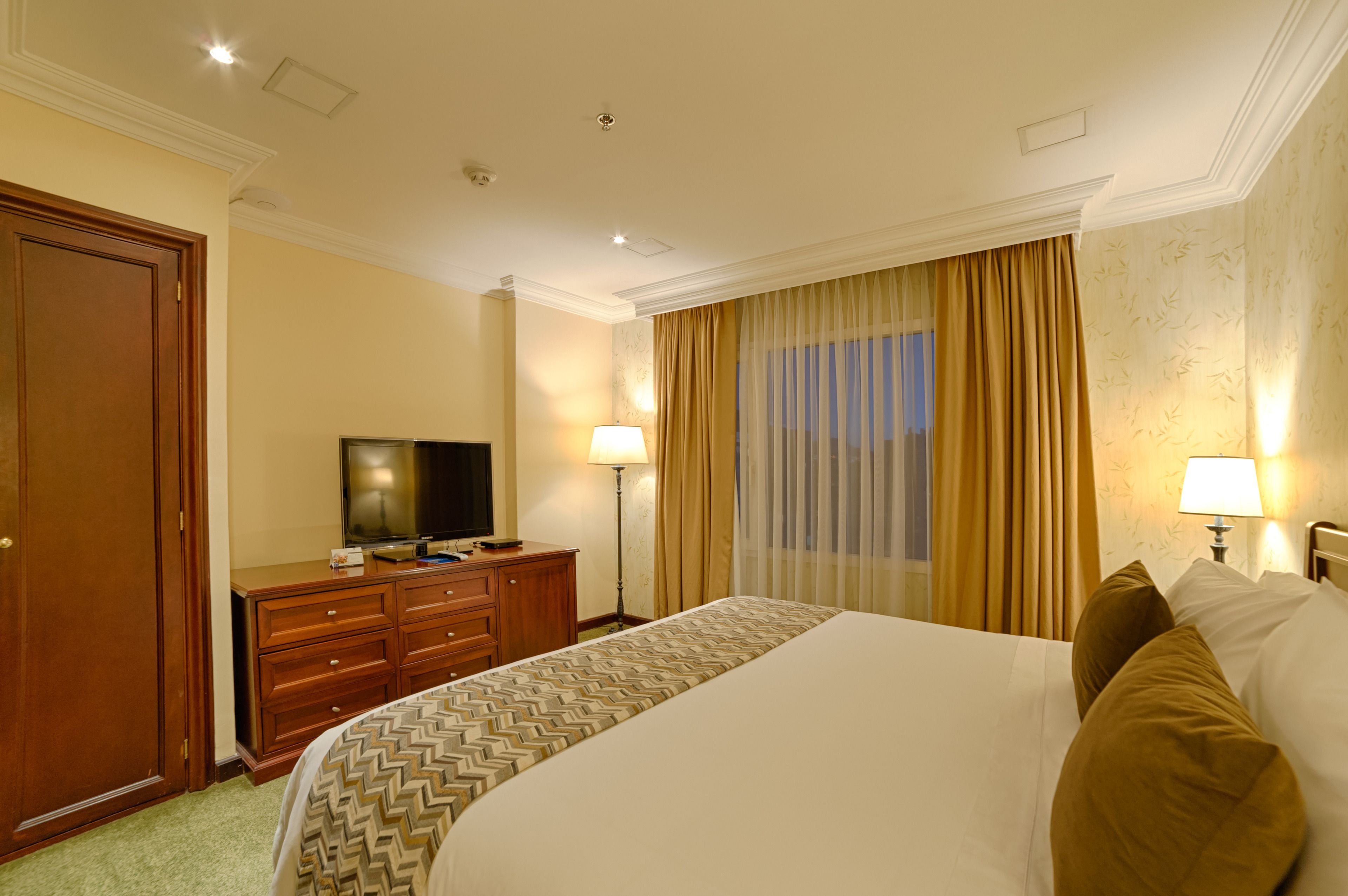 Una habitación de hotel con una cama grande, un televisor sobre un aparador de madera y una ventana con cortinas.