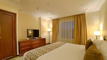 Una habitación de hotel con una cama grande, un televisor sobre un aparador de madera y una ventana con cortinas.
