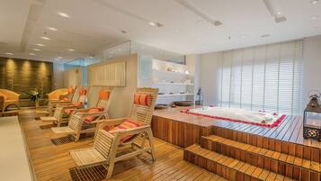 Uma área de spa com piso de madeira, cadeiras acolchoadas, uma banheira de hidromassagem e uma escadaria para um andar superior.