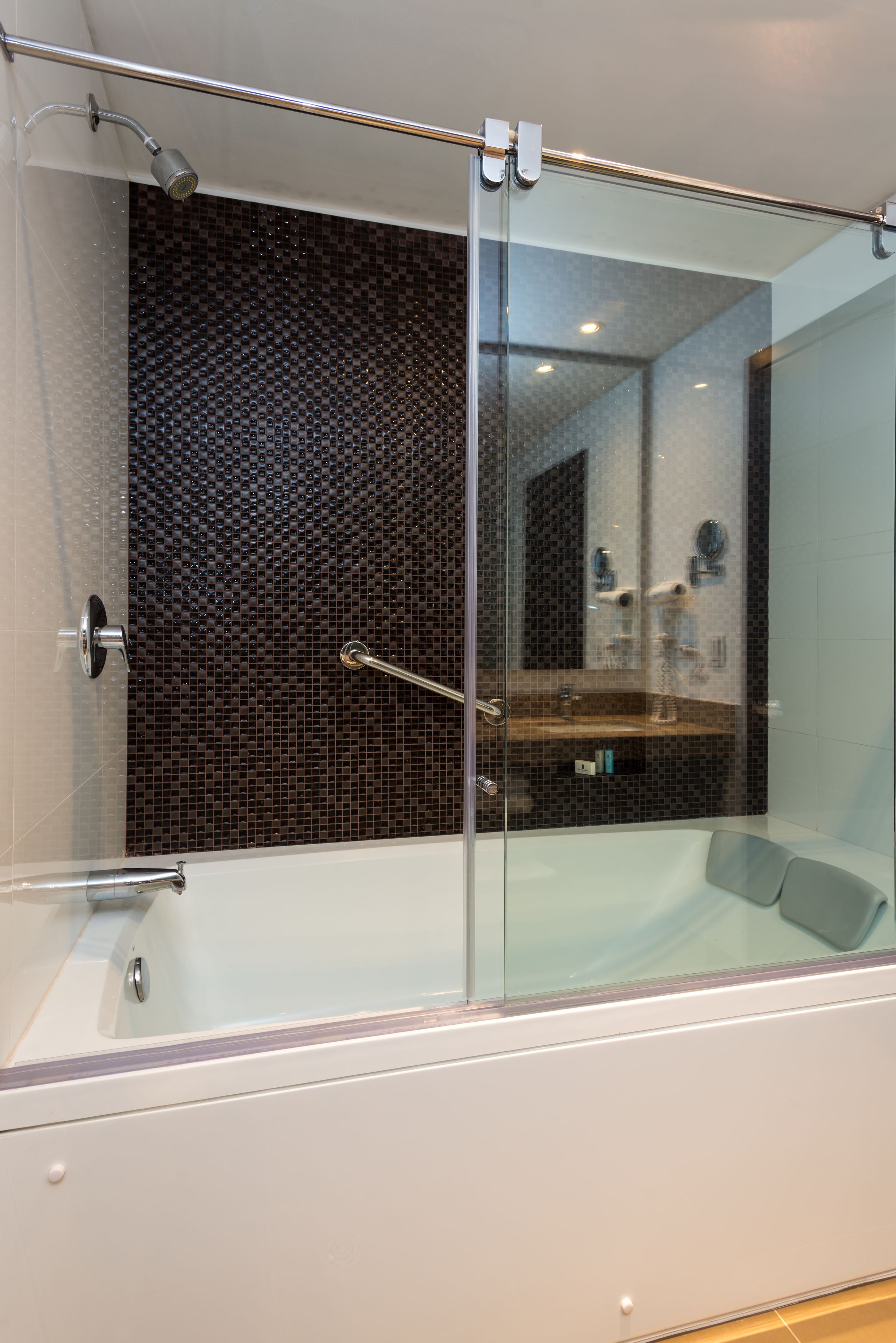A modern bathroom with a glass-enclosed shower, a white bathtub, and a dark mosaic wall.
