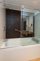 Un baño moderno con ducha acristalada, una bañera blanca y una pared de mosaico oscuro.