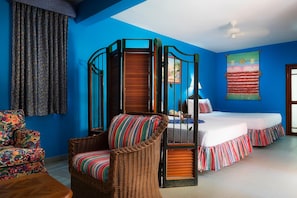 A room with a blue wall, a wicker chair, a bed with a striped bedspread, and a window with a view of a landscape.