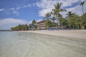 Een strandhotel met helder water, palmbomen en een gebouw met meerdere balkons.