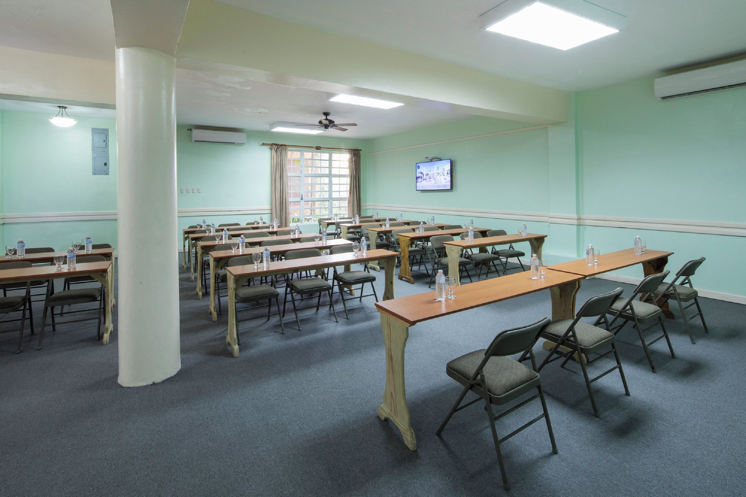 Una sala conferenze con diversi tavoli e sedie, una ventola a soffitto e un televisore appeso al muro.