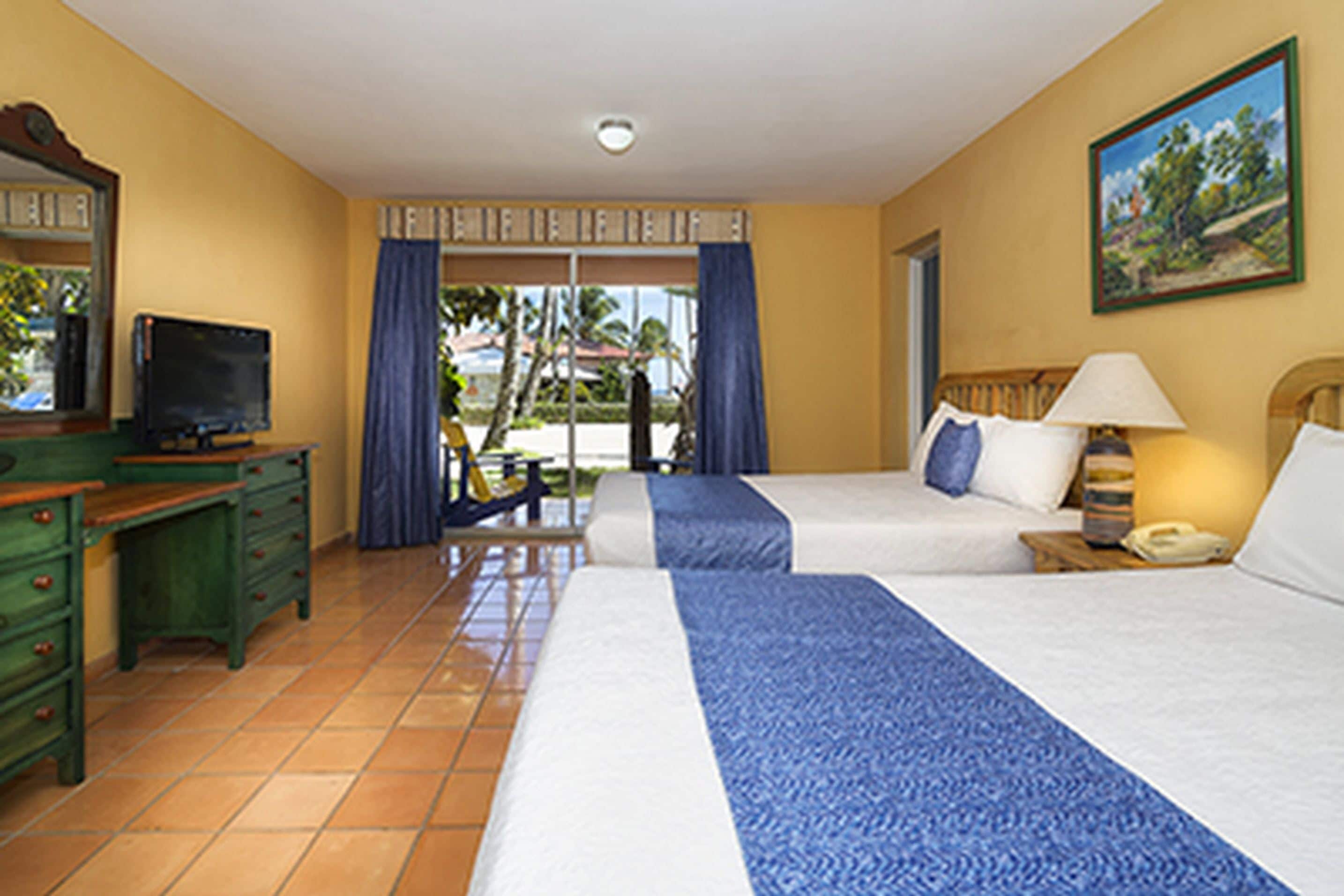 A hotel room with a bed, a desk with a television, a chair, and a window with curtains.
