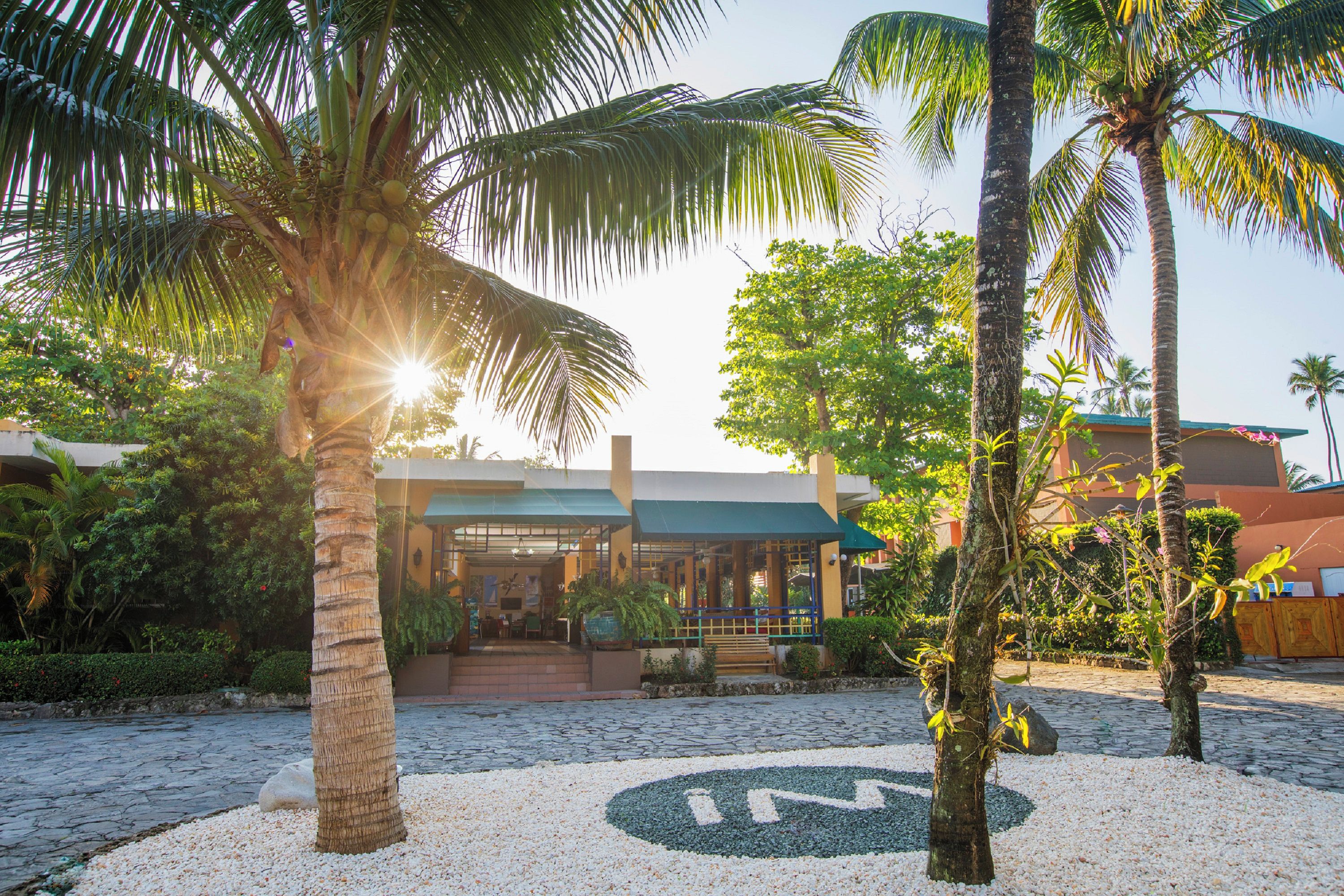 Un complexe hôtelier tropical doté de palmiers, d’un sentier pavé et d’un bâtiment surmonté d’un toit végétalisé.