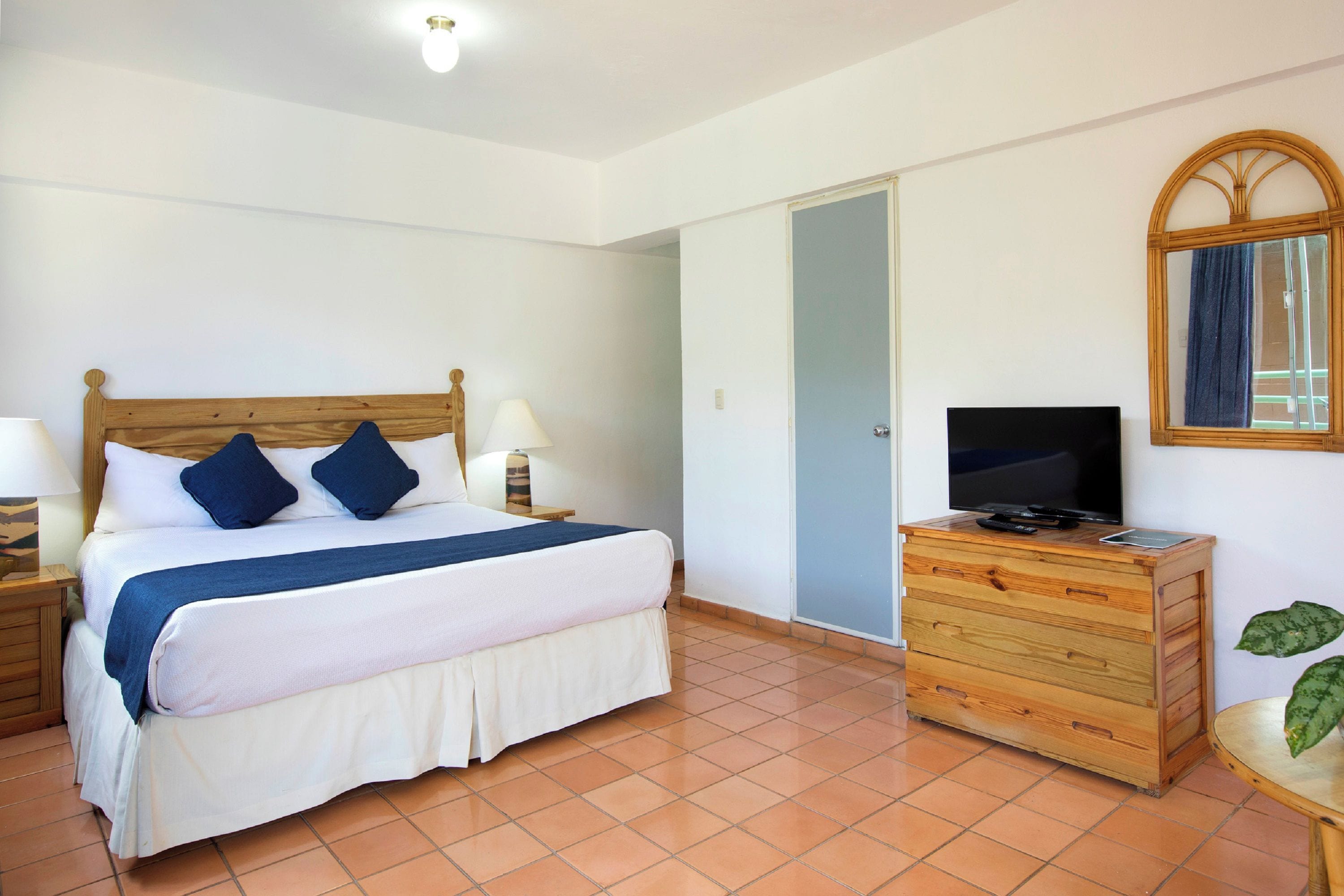Une chambre  à coucher avec un lit, une commode en bois, un téléviseur et une fenêtre avec un rideau.