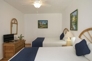Un dormitorio con dos camas, un aparador de madera con un televisor, un ventilador de techo y dos cuadros en la pared.