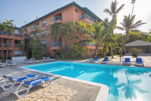 A hotel with a swimming pool, lounge chairs, and palm trees.