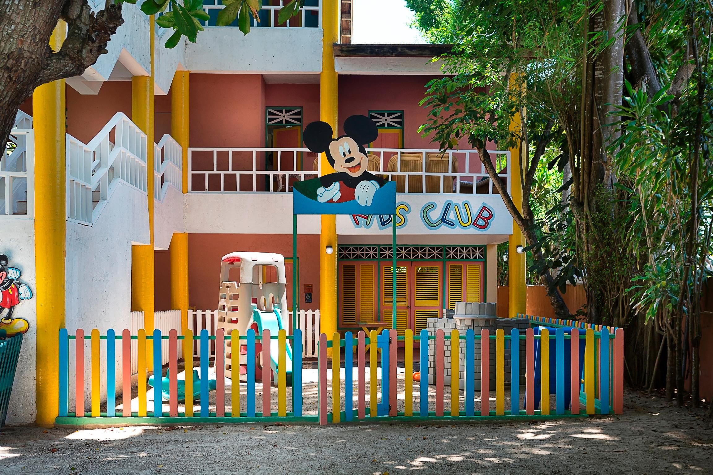 Un club pour enfants avec une clôture colorée, un toboggan et un panneau à l’effigie de Mickey Mouse.