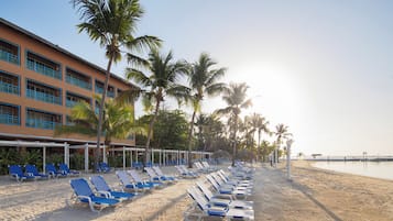 Ein Hotel direkt am Strand mit Liegestühlen und Palmen.