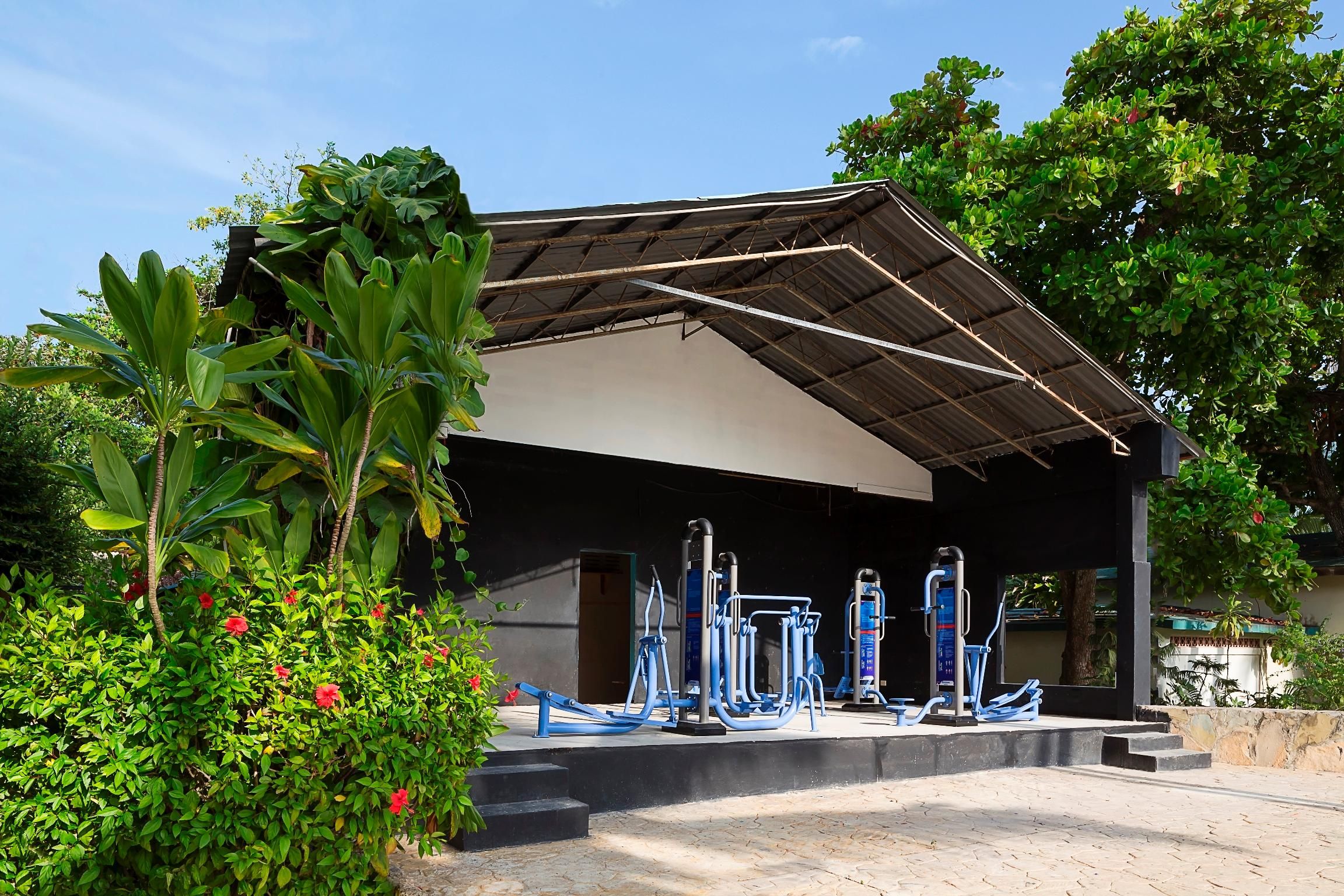 Area fitness esterna con attrezzature, immersa nel verde e riparata da una struttura coperta.