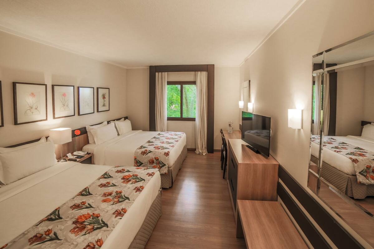 A hotel room with two beds, a desk, a TV, and a large mirror.