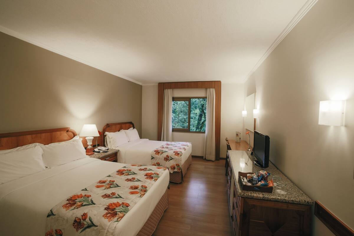 A hotel room with two beds, a television, a desk, and a window with curtains.