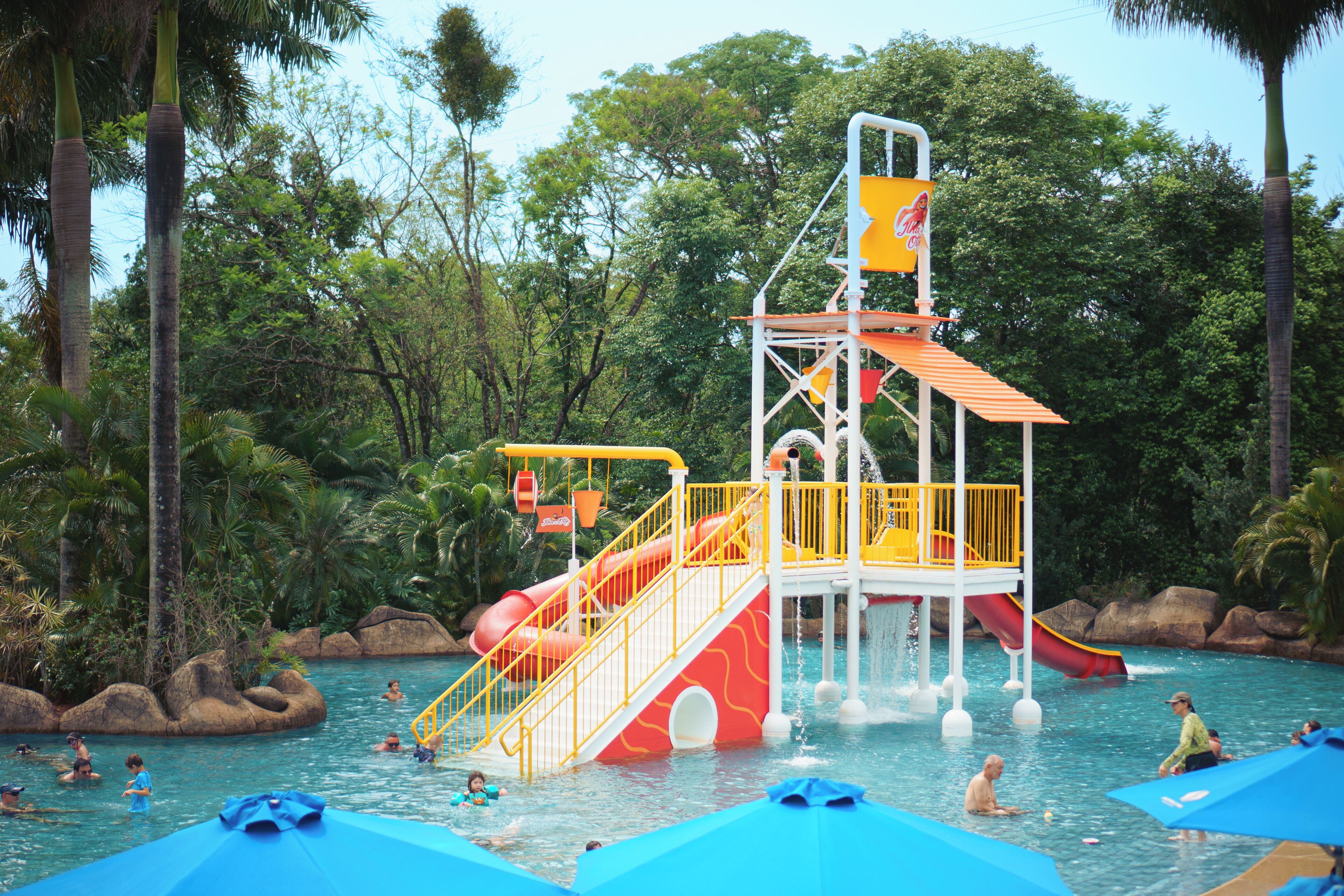 Un parque acuático con toboganes, una torre de salvavidas y gente nadando.