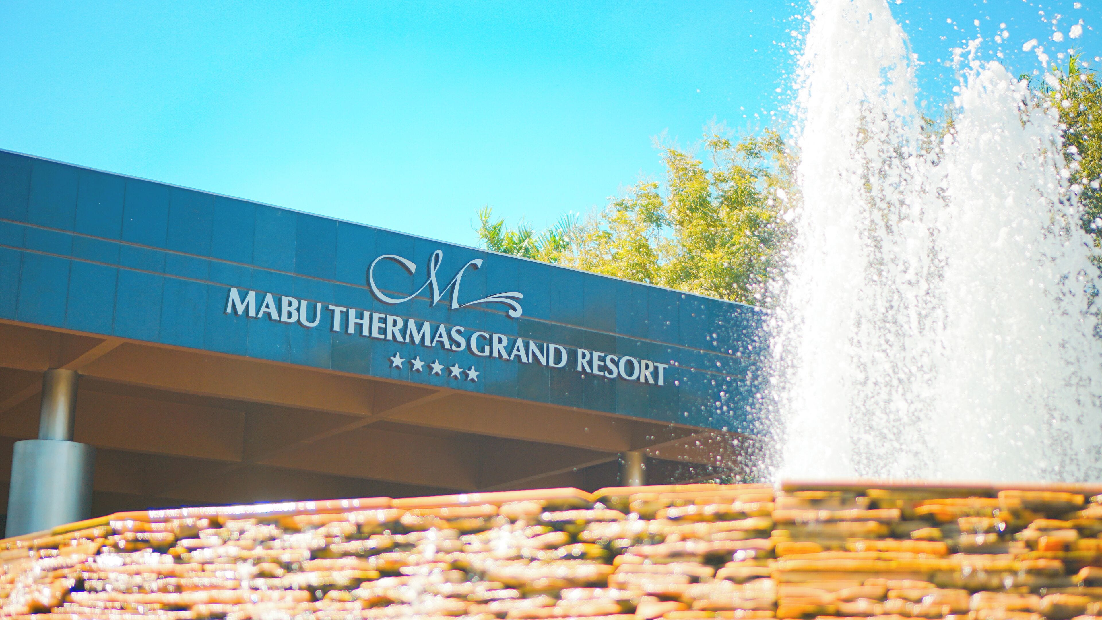 Een bordje voor Mabu Thermas Grand Resort met een waterfontein op de voorgrond.
