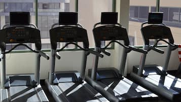 Trois tapis de course dans une salle de sport, avec vue sur les bâtiments environnants.
