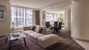 Een moderne woonkamer met een beige bank, een glazen salontafel en een eethoek met een tafel en stoelen.