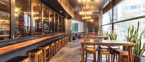 Un restaurante moderno con muebles de madera, amplios ventanales y plantas de interior.