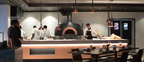 Una cocina moderna con horno de ladrillo, lámparas colgantes y un comedor con mesas y sillas.