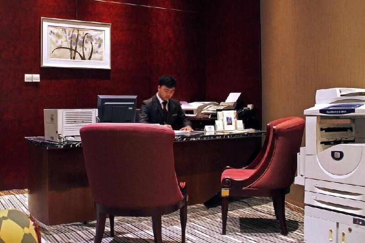 A hotel reception desk with a computer, printer, and a framed artwork on the wall.