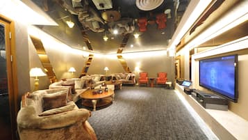 En hotelbar med sofaer, lænestole, et sofabord, et fjernsyn og et loft med unik indretning.