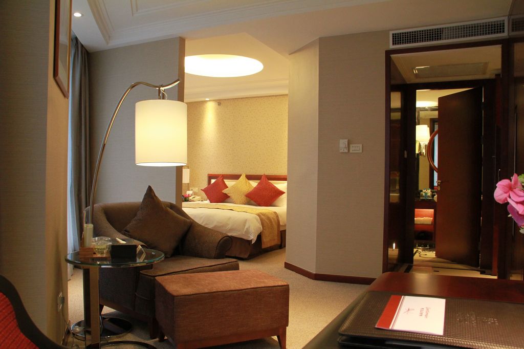 A hotel room with a bed, a sofa, a small table, and a lamp.