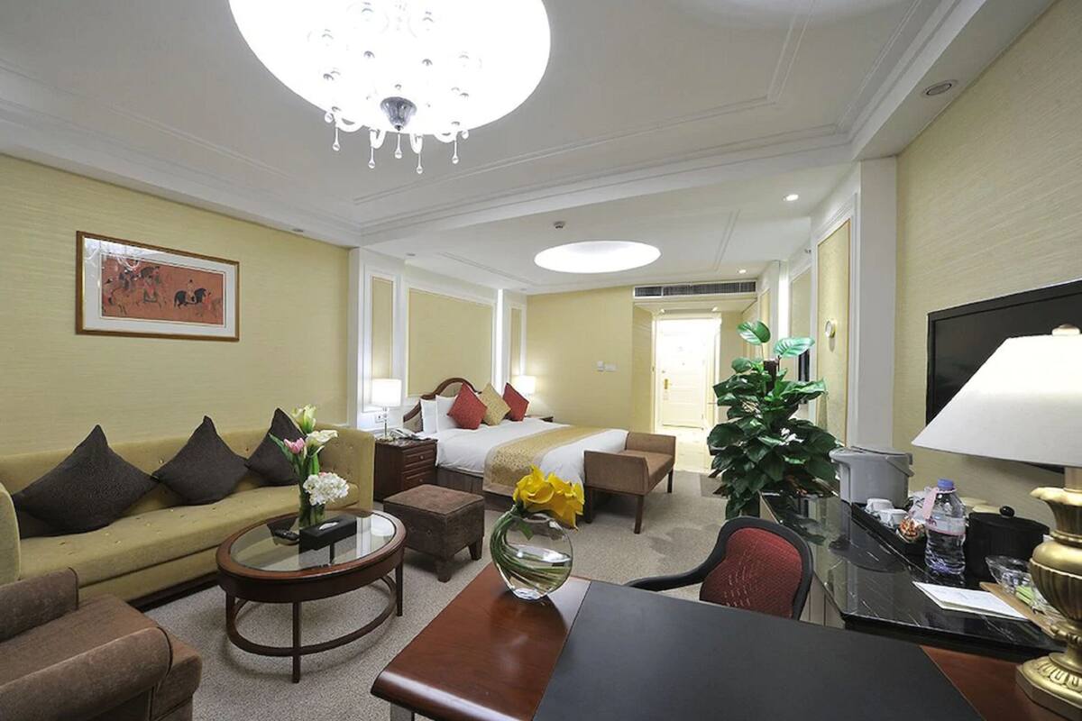 Quarto de hotel com cama, sofá, mesa de centro, escrivaninha e televisão.