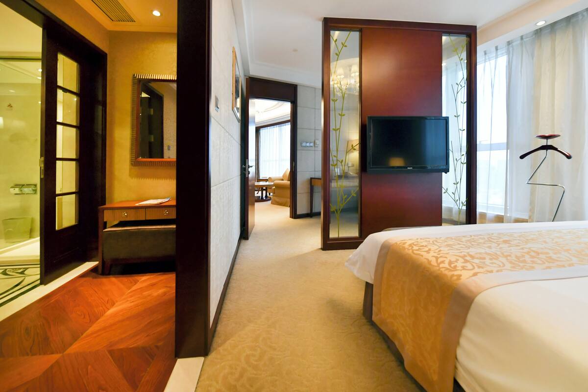 Quarto de hotel com uma cama grande, televisão, escrivaninha e banheiro com espelho e pia.