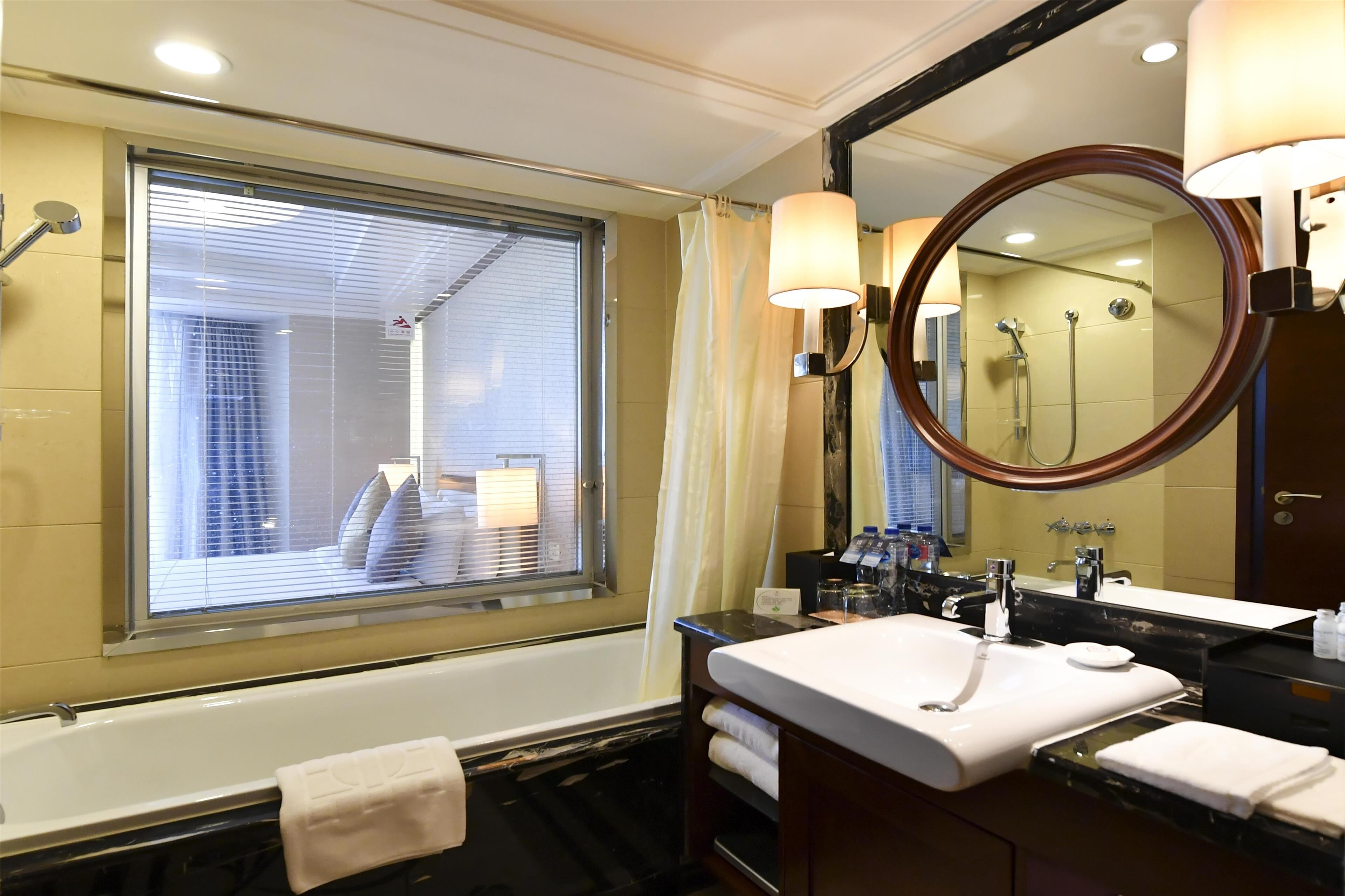 A bathroom with a bathtub, a sink, a mirror, and a window with blinds.