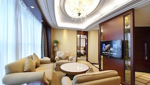 A hotel room with a sofa set, a round coffee table, a TV mounted on the wall, and a large window with curtains. - Central Hotel Shanghai (Shanghai)
