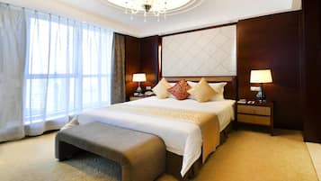 A hotel room with a large bed, two bedside tables with lamps, a bench, and a large window with curtains.