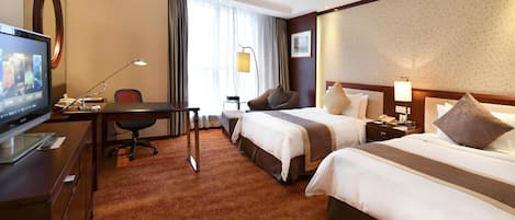 A hotel room with two beds, a desk with a computer, a TV, and a large window with curtains.