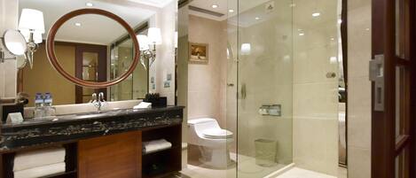 Un baño moderno con ducha envuelta en cristal, un espejo grande con apliques de pared y encimera de mármol.