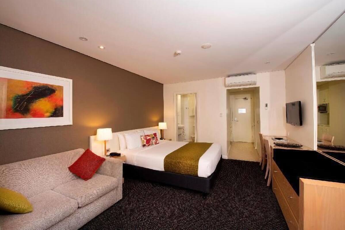 A hotel room with a bed, a sofa, a desk, and a television.