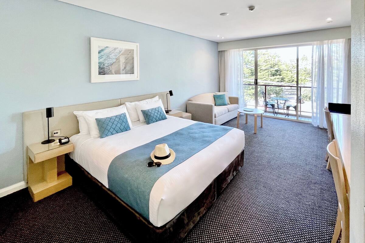 A hotel room with a large bed, a sofa, a small table, and a balcony with a view.