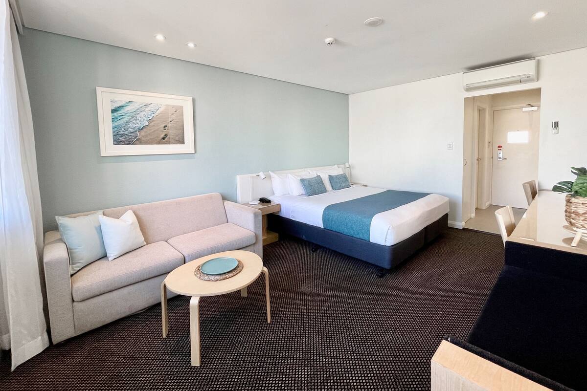 A hotel room with a bed, a sofa, a small table, and a desk.