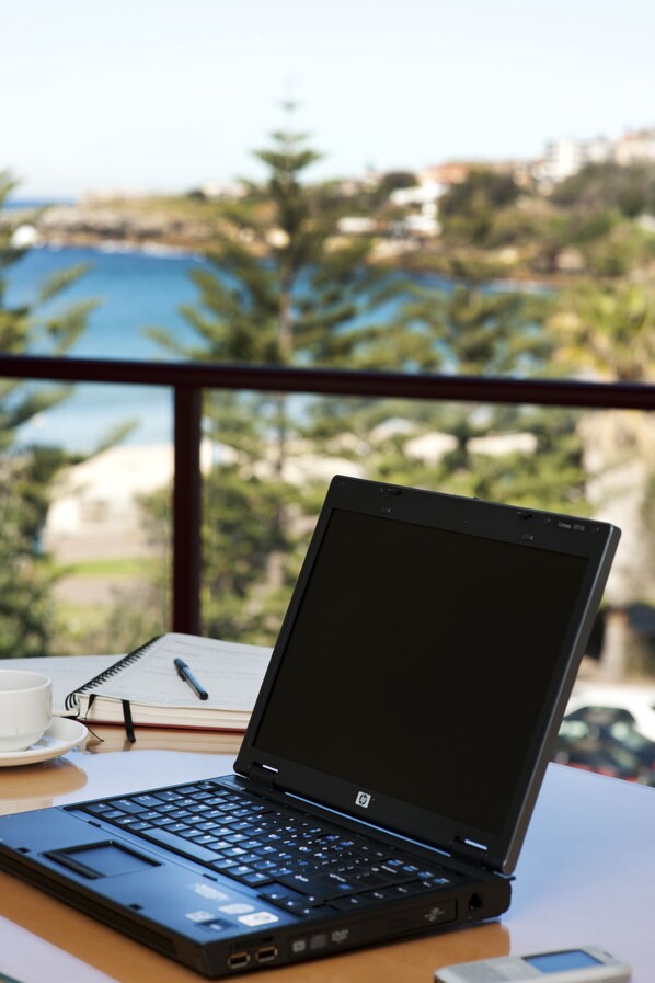 A laptop on a desk with a notebook, pen, and a cup. - Coogee Sands Hotel & Apartments (Sydney)