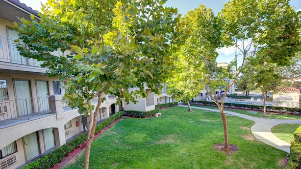 A courtyard with a grassy lawn, trees, and a building with balconies and windows.