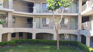 A multi-story residential building with balconies, arched doorways, and a well-maintained lawn.