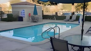 A swimming pool with a glass edge, surrounded by lounge chairs and a table with a glass top.
